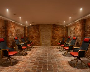 Ein Raum mit mehreren roten und schwarzen Stühlen, die in zwei Reihen auf einem gefliesten Boden angeordnet sind. Beleuchtet von Deckenlichtern.