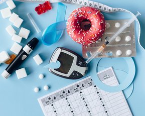 Diabetesbedarf: Blutzuckermessgerät, Insulinspritzen, Medikamente, Zuckerwürfel, eine Donut und ein Diabetes-Tagebuch auf einem blauen Hintergrund.