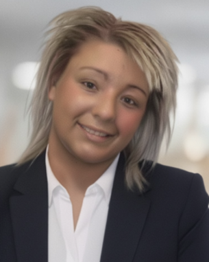 Eine Person mit blonden, schulterlangen Haaren trägt einen schwarzen Anzug und lächelt freundlich in einem modernen Büro.