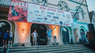 Eine Bühne mit einem Redner und mehreren Personen, umgeben von Sponsorenbanner für die Veranstaltung "BW Open 2026".