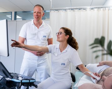 Kardiologie-innere Medizin Zwei medizinische Fachkräfte in weißen Uniformen stehen vor einem Monitor. Eine Person zeigt auf den Bildschirm, während die andere aufmerksam zuschaut.