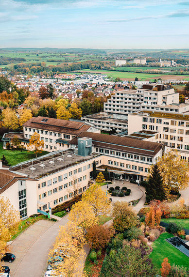 Ein weitläufiges Gebäudeensemble in einer herbstlichen Landschaft, umgeben von bunten Bäumen. Die Architektur umfasst mehrere miteinander verbundene Gebäude, die in einem ruhigen, ländlichen Gebiet liegen.
