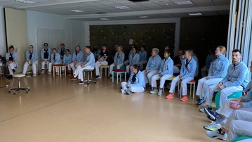 Eine Gruppe von Menschen in blauen Arbeitskleidung sitzt in einem Raum auf Stühlen und hört einem Vortrag zu.